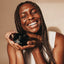 Black woman smiling holding UMM Skincare's body scrub to gently exfoliate her skin.