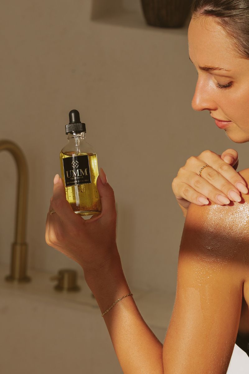 Woman applying UMM Skincare pre shower body oil to her arms. 