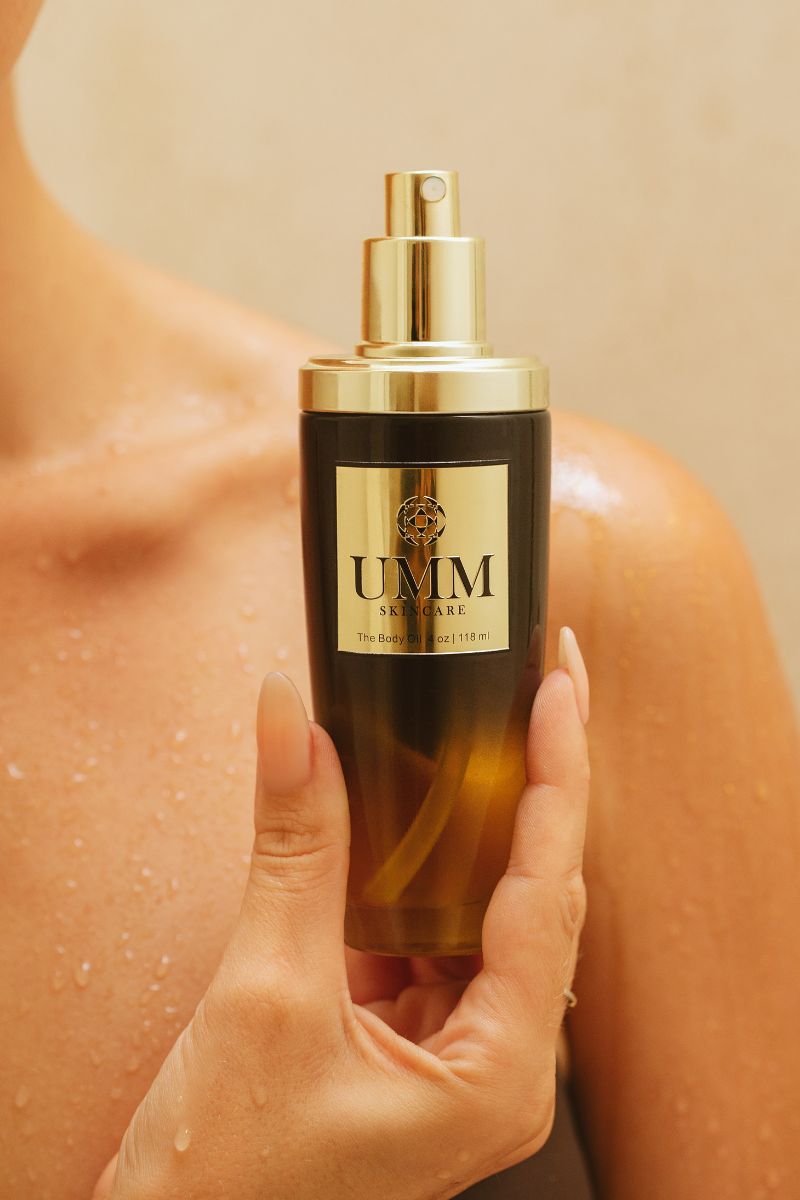 Woman holding UMM Skincare post shower body oil in front of wet skin.