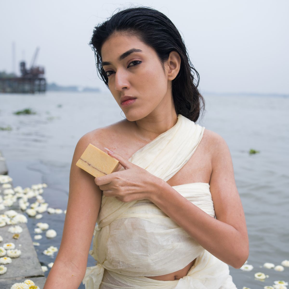 Woman using UMM Skincare soap bar to cleanse her shoulder, standing by the water with a serene and confident expression, showcasing luxury Ayurvedic beauty.