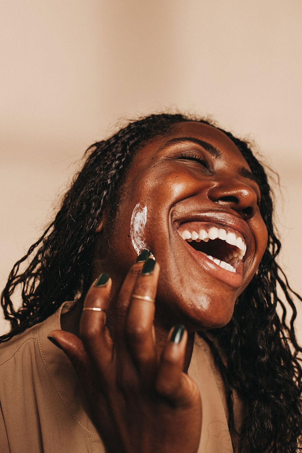 Black woman laughing and smiling as she applies moisturizing cream to her ace.